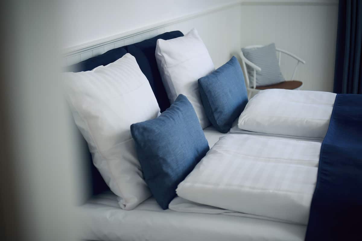 A neatly made bed with white and blue bedding, a white headboard, and a chair with a striped pillow.