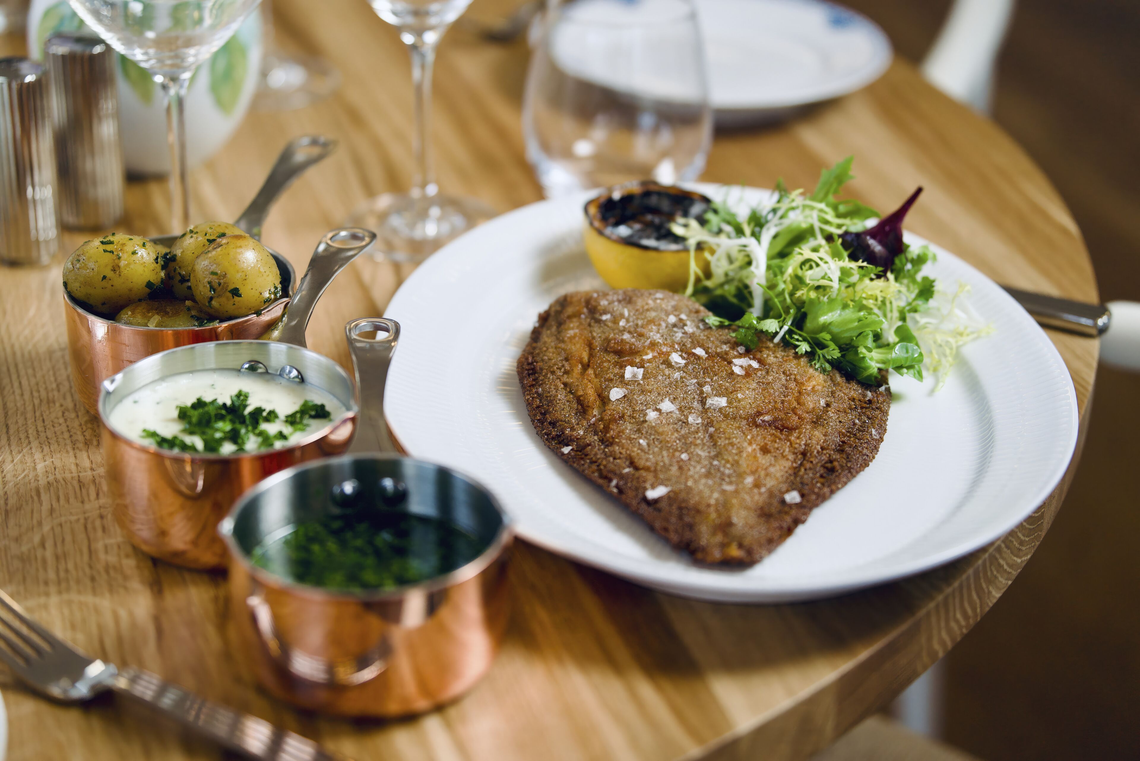 Un plato con milanesa, ensalada y patatas sobre una mesa de madera.