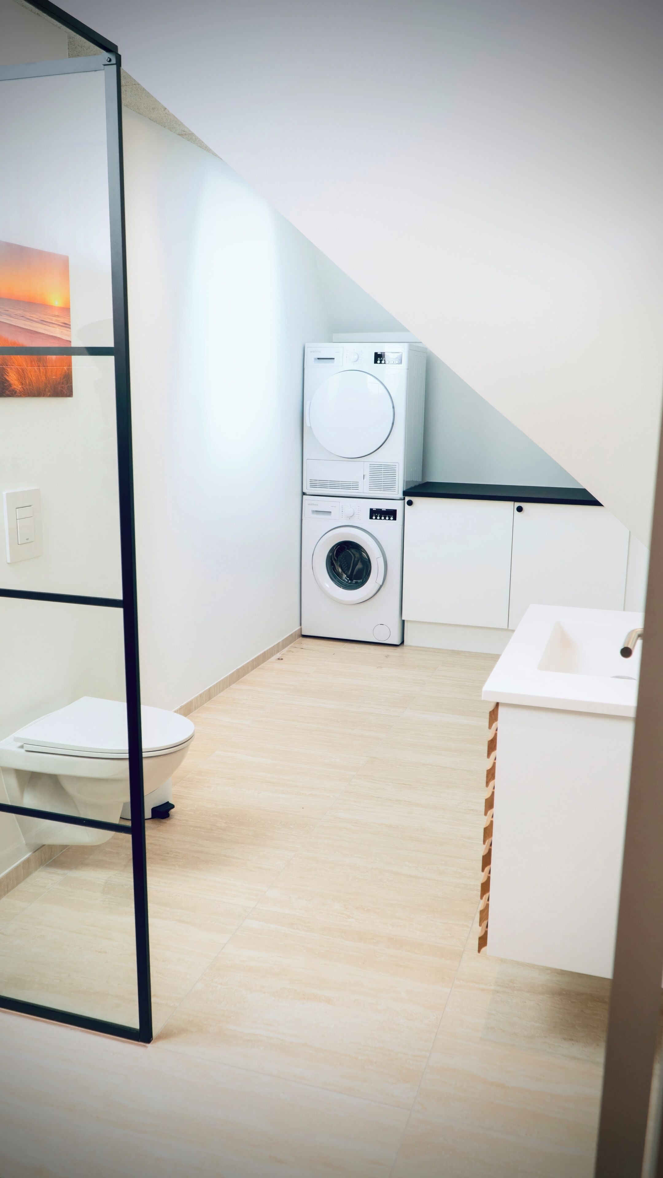 A compact, modern bathroom with a washing machine, toilet, and sink.