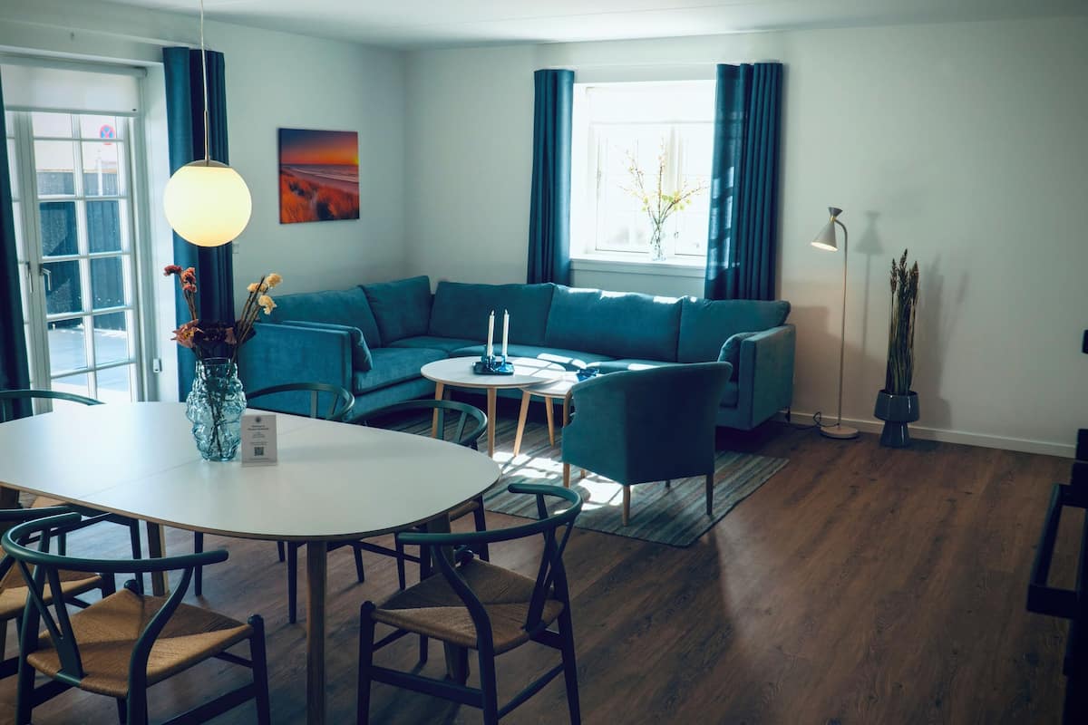 A modern living room with a blue sofa, a round dining table with chairs, and a vase with flowers.