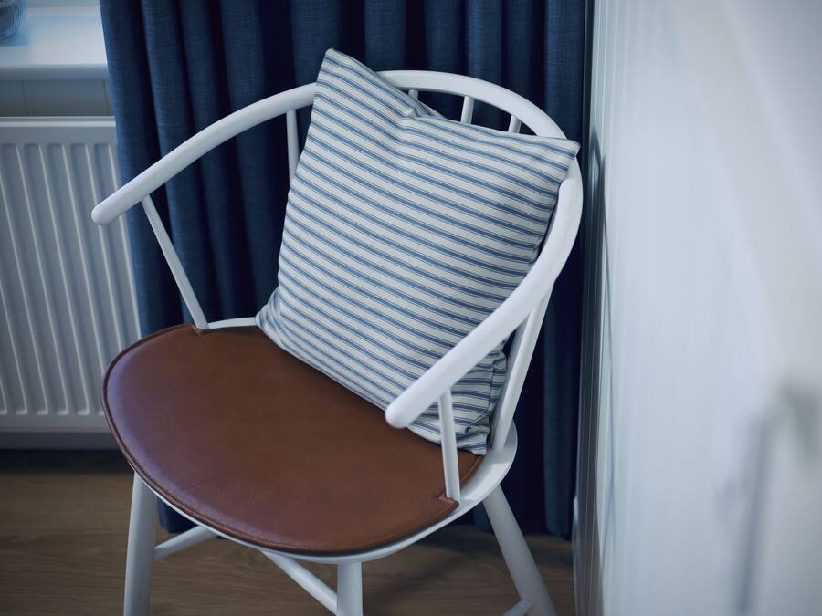 A white chair with a brown seat and a striped pillow.