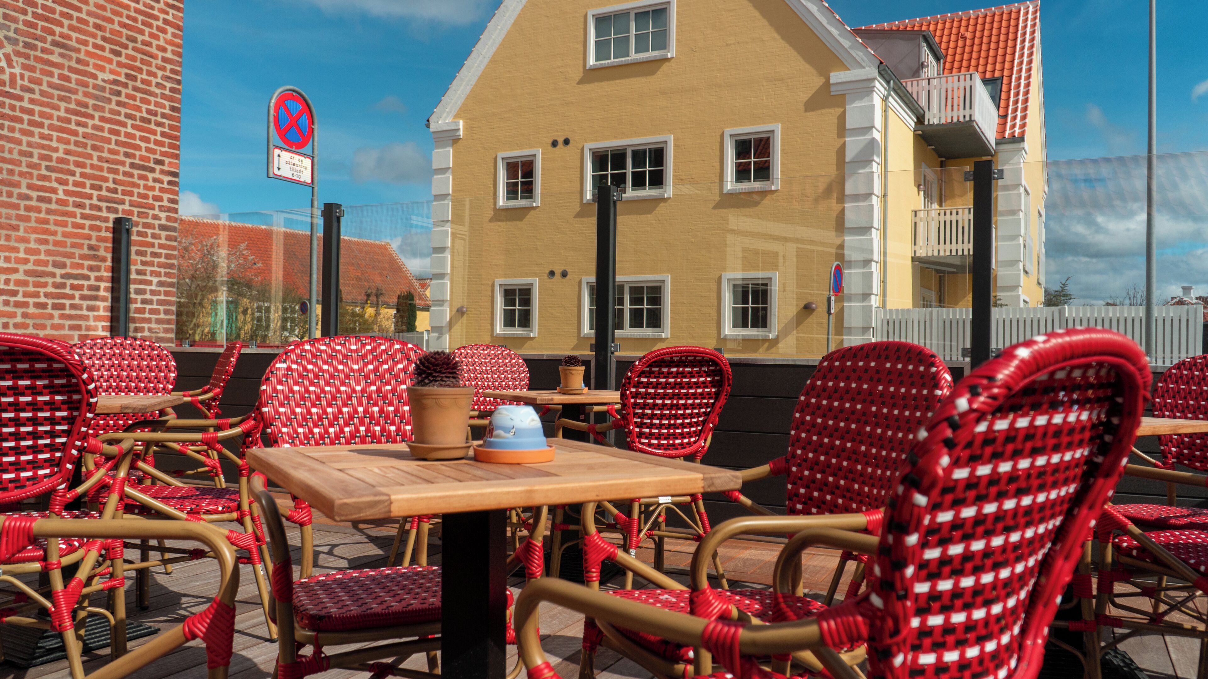 Outdoor seating with wicker chairs and a table, a building with a yellow facade, and a no parking sign in the background.