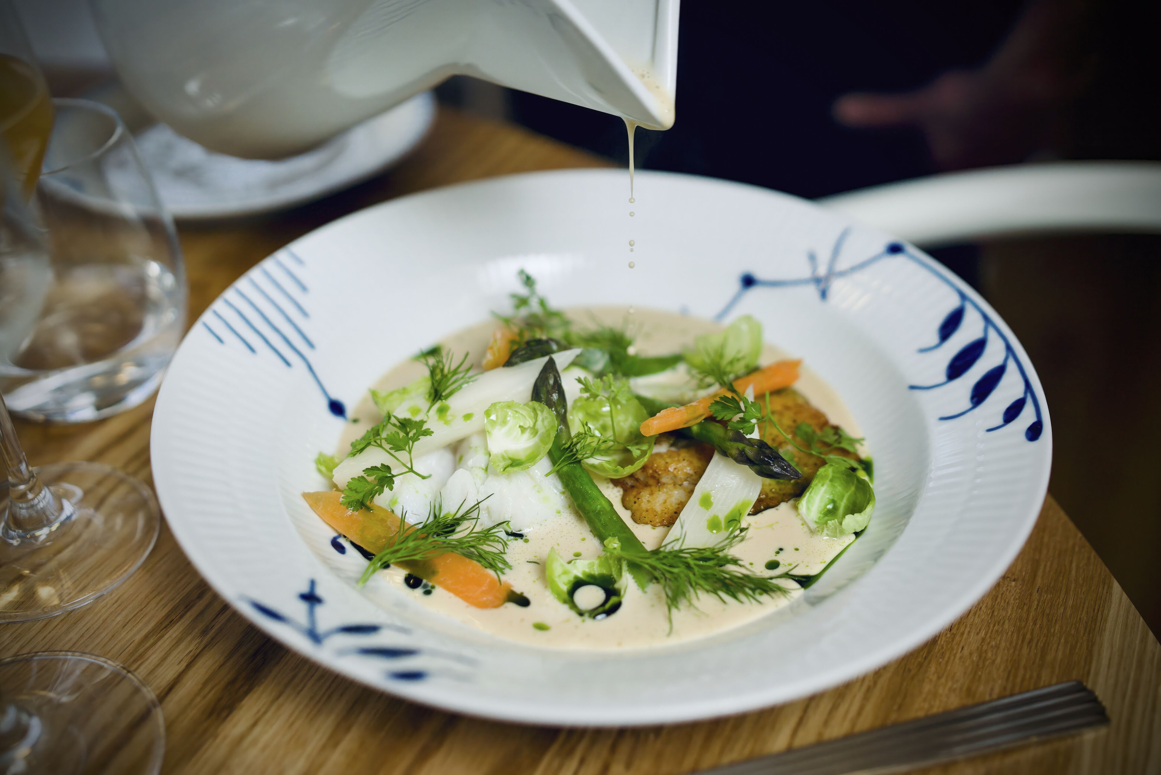 Une assiette de nourriture comprenant divers légumes et une sauce crémeuse, servie dans une assiette blanche ornée de motifs bleus.