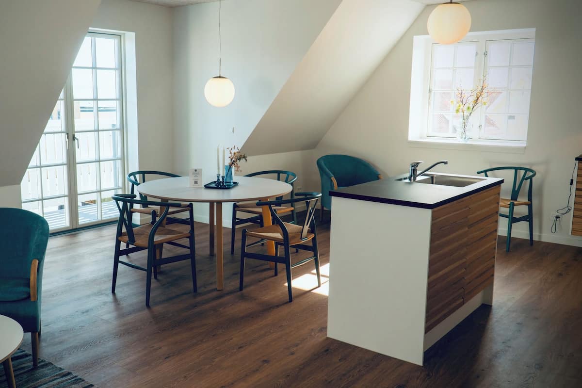 A modern kitchen with a central island, wooden flooring, and a dining area with chairs and a table.