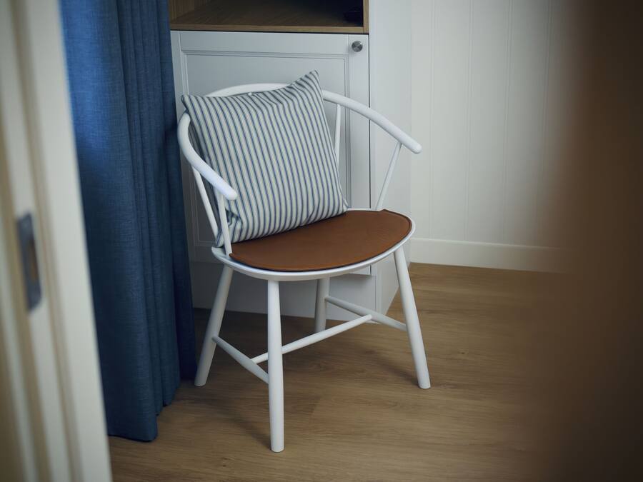 En hvid stol med pude med striber og brunt sæde, placeret i et rum med trægulv og en hvid dør.