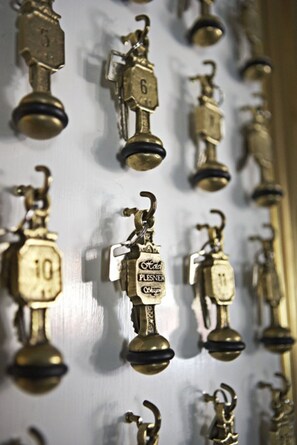 A wall of brass door knockers with numbers and the word "PLEASER" visible.