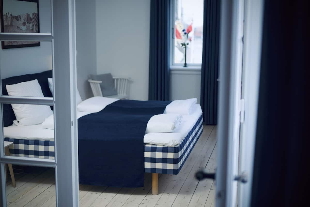 A hotel room with a bed, a chair, a window with curtains, and a radiator.