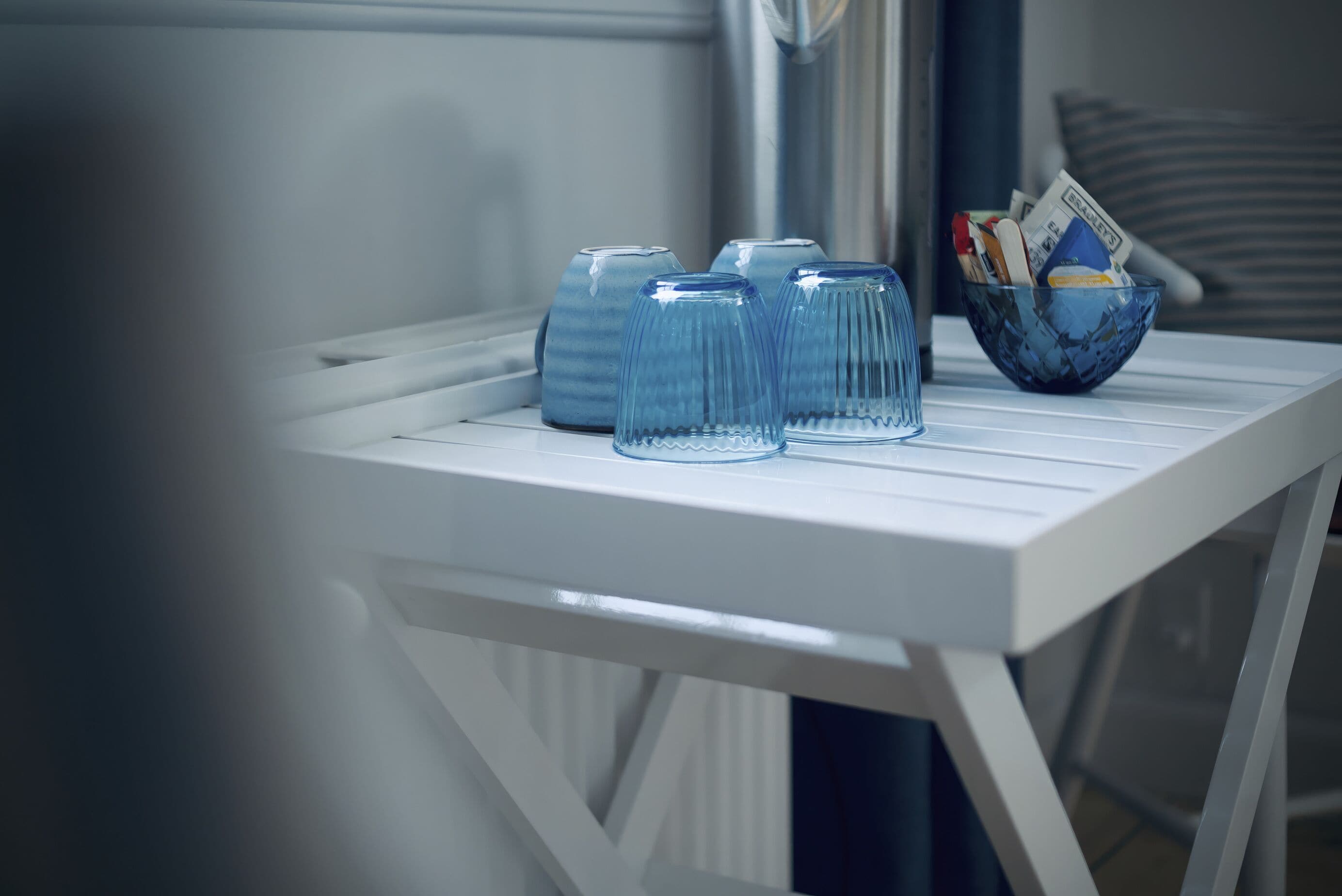 A white table with four blue glass tumblers and a blue bowl containing books and money.