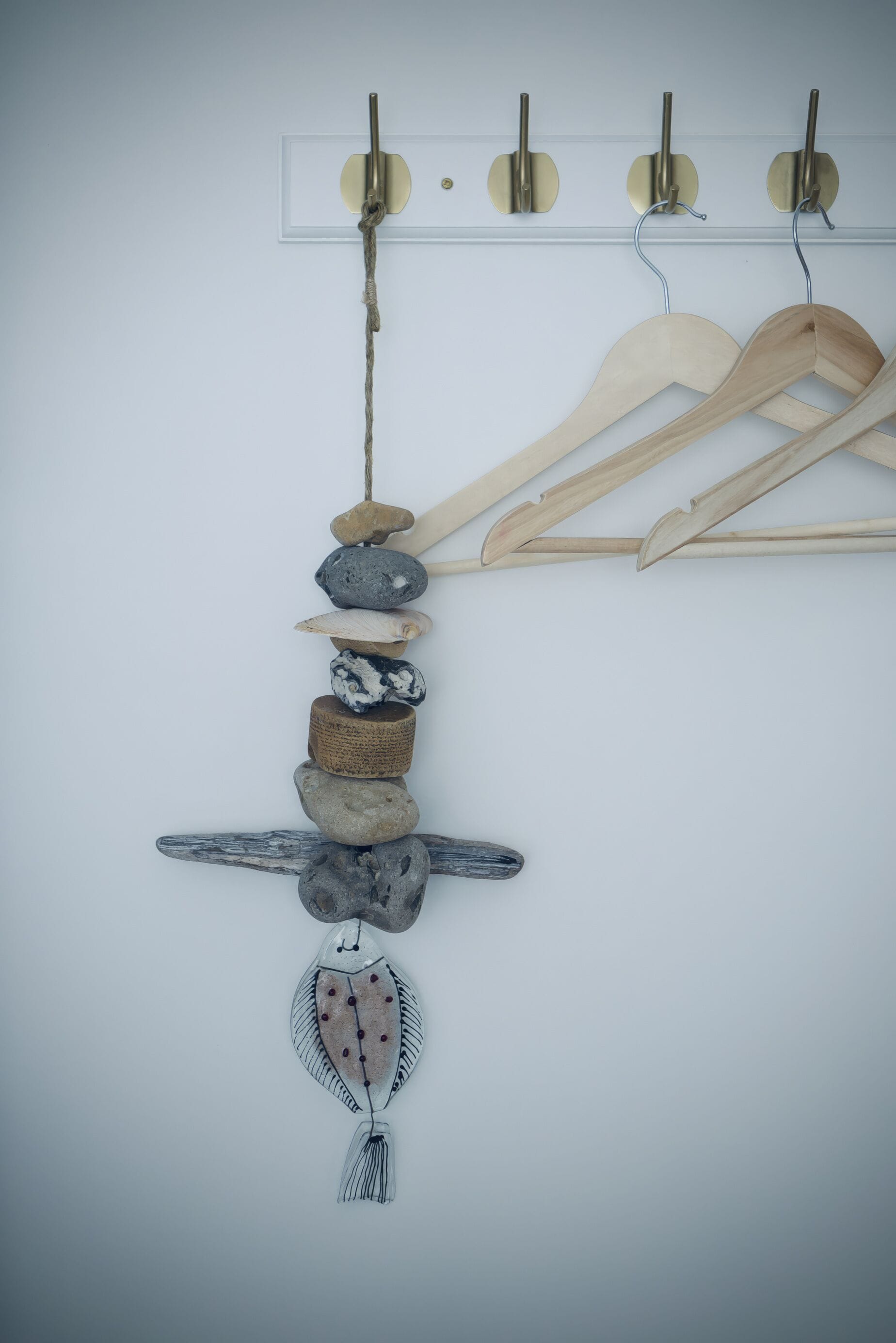 A wall-mounted rack with wooden hangers and a decorative arrangement of stones and a fish-shaped ornament.