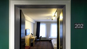 A hotel room with a bed, a desk, a chair, a TV, and a window with curtains. - Hotel Ambassador Essen (Essen)