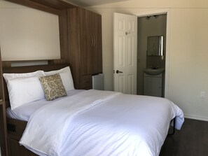 Un dormitorio con una cama grande, un armario de madera y un baño visible a través de una puerta abierta.