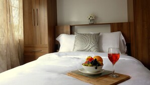 Una cama bien hecha con sábanas blancas, un cuenco de fruta y un vaso de bebida roja sobre una bandeja de madera.