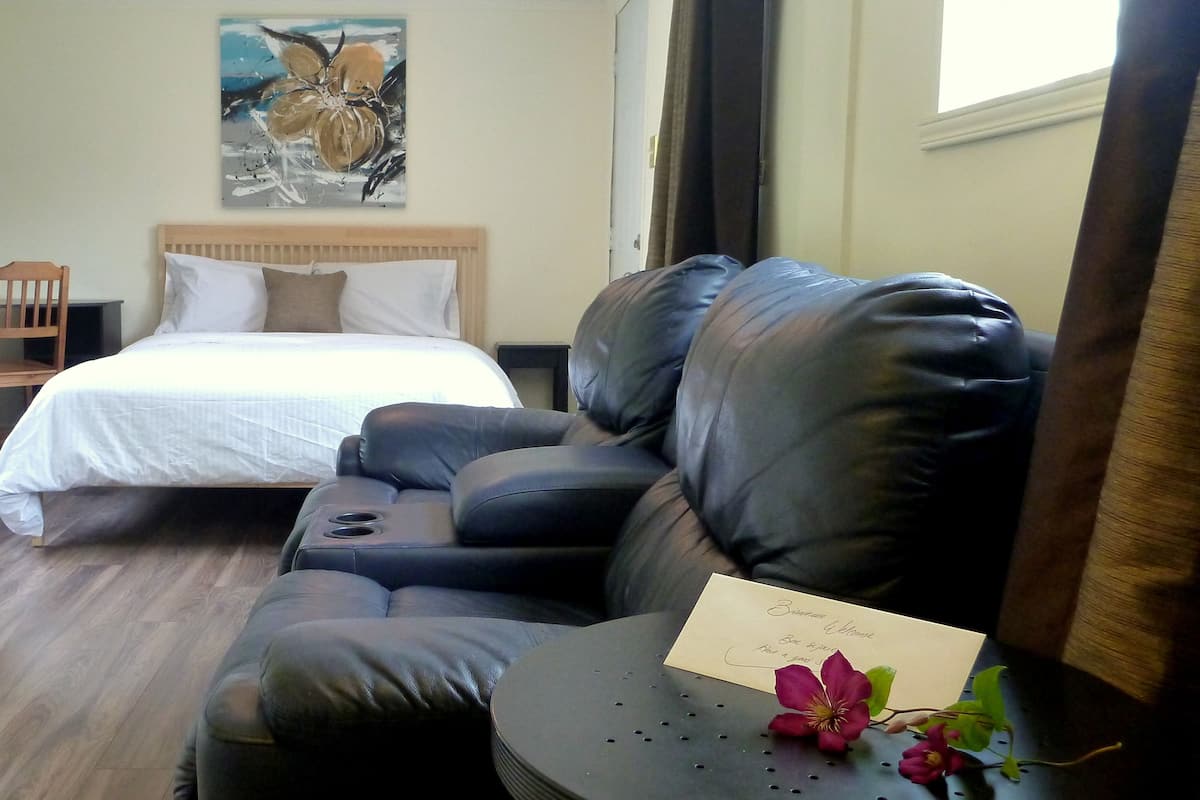 Una habitación de hotel con una cama, un sofá de cuero, una mesita con una tarjeta de bienvenida y un cuadro en la pared.