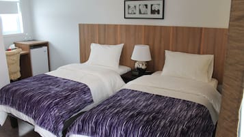 Een kamer met twee bedden, een klein bureau met een lamp en een koelkast.