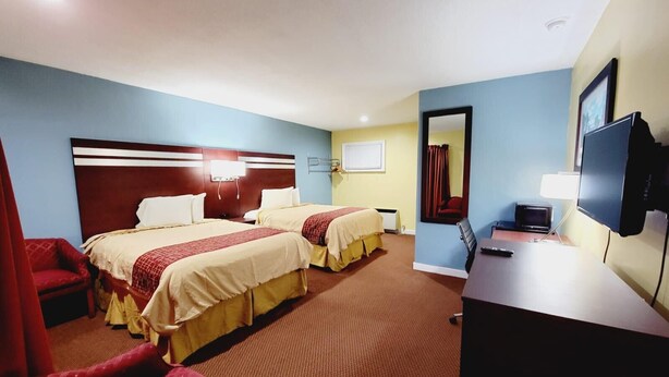 A hotel room with two beds, a desk, a chair, a TV, and a mirror. - Bassett Motel (Williamsburg)