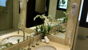 A hotel bathroom with two sinks, a large mirror, and a hairdryer mounted on the wall.
