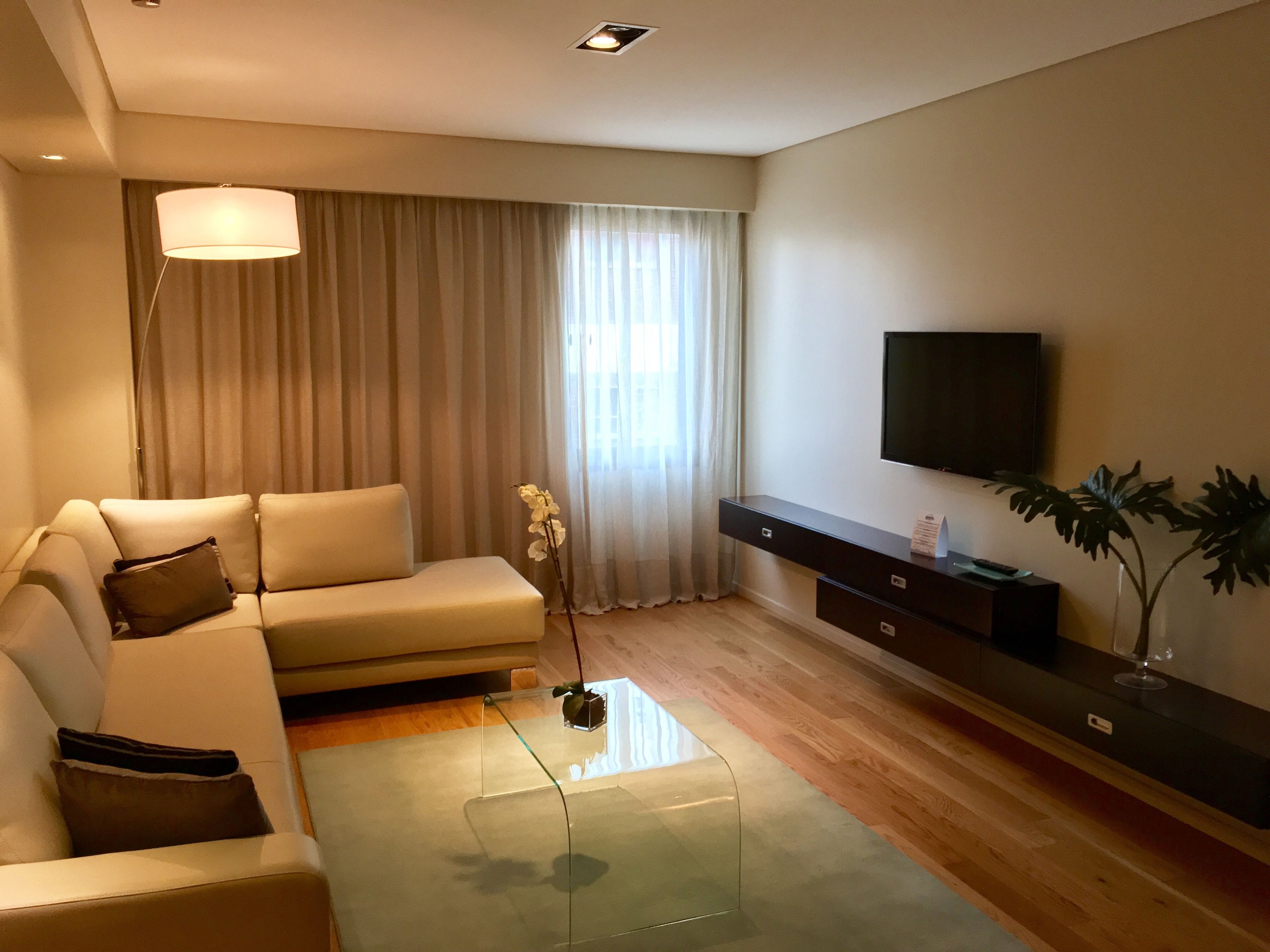 Ein modernes Wohnzimmer mit einer Couch, einem Glastisch, einem Flachbildfernseher und einer Pflanze.