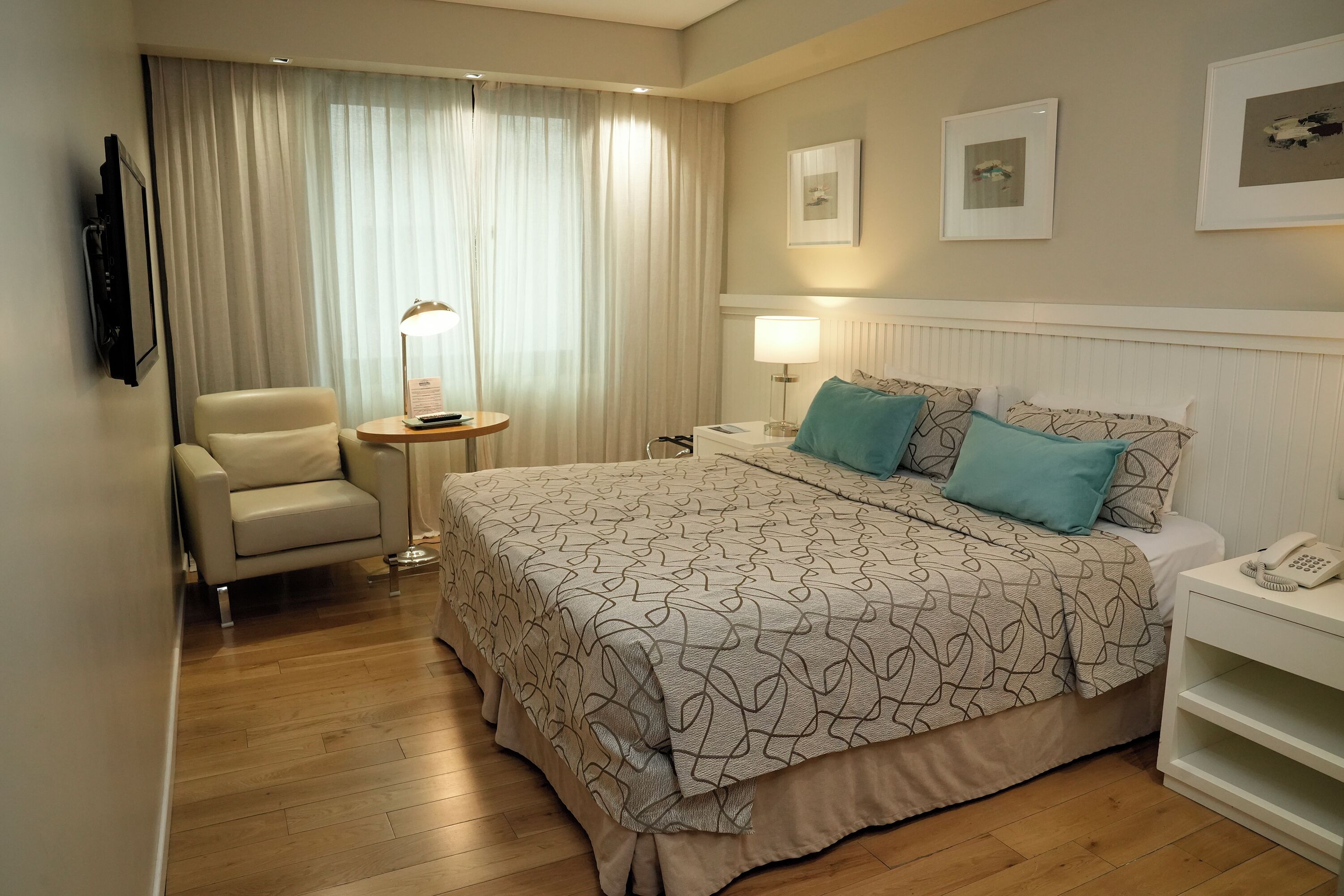 Una habitación de hotel con cama, una silla, mesita de noche, lámpara y teléfono.