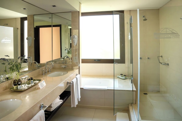 A modern bathroom with dual sinks, a large mirror, a glass-enclosed shower, and a bathtub. - Hotel Metropolitano Supara (Buenos Aires)