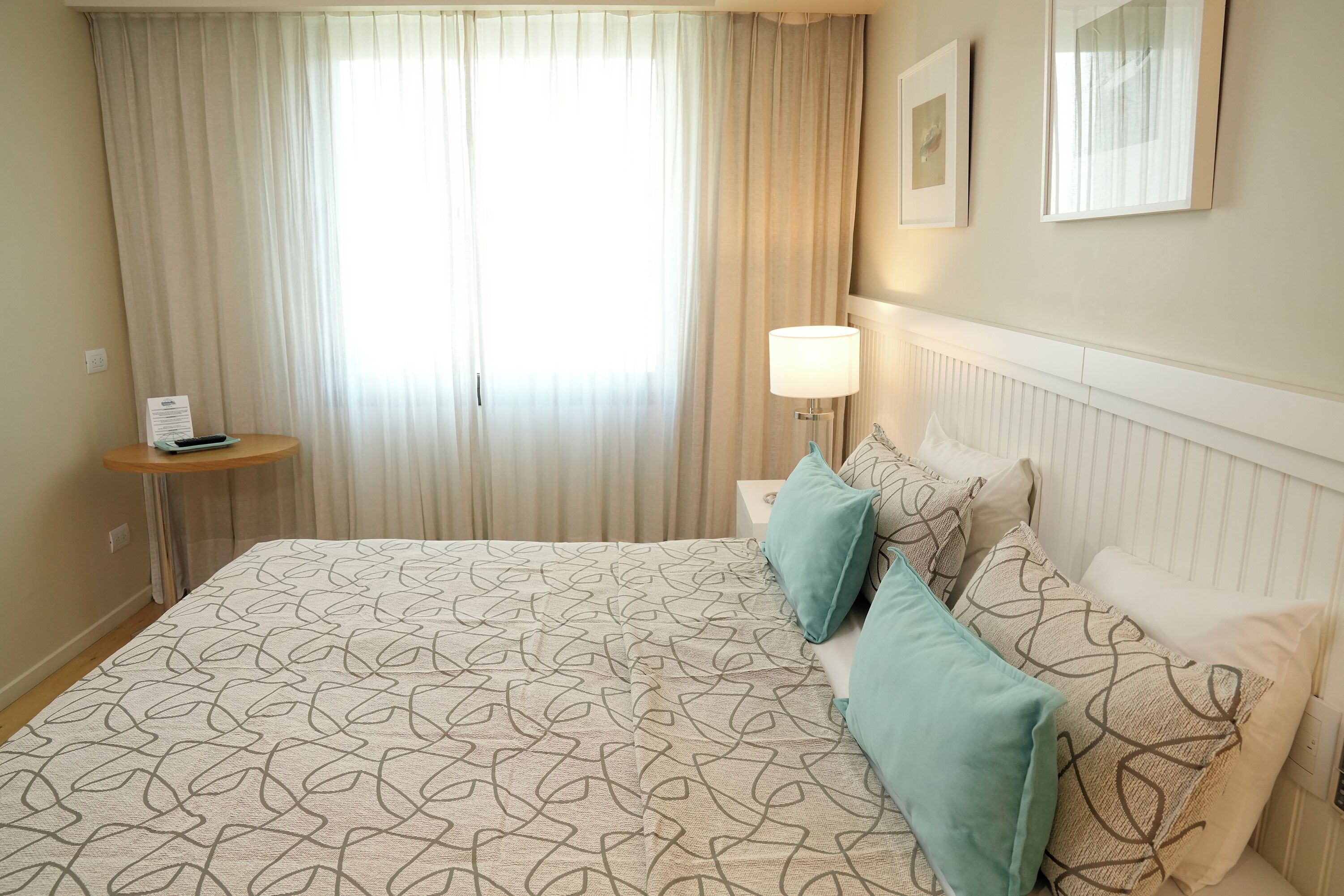 Habitación de hotel con una cama grande, una mesita de noche, una lámpara y una ventana con cortinas.