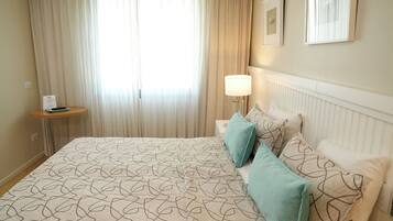 Habitación de hotel con una cama grande, una mesita de noche, una lámpara y una ventana con cortinas.