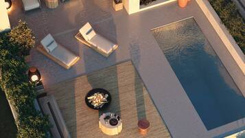 An aerial view of a pool area with lounge chairs, a fire pit, and a small table with drinks.
