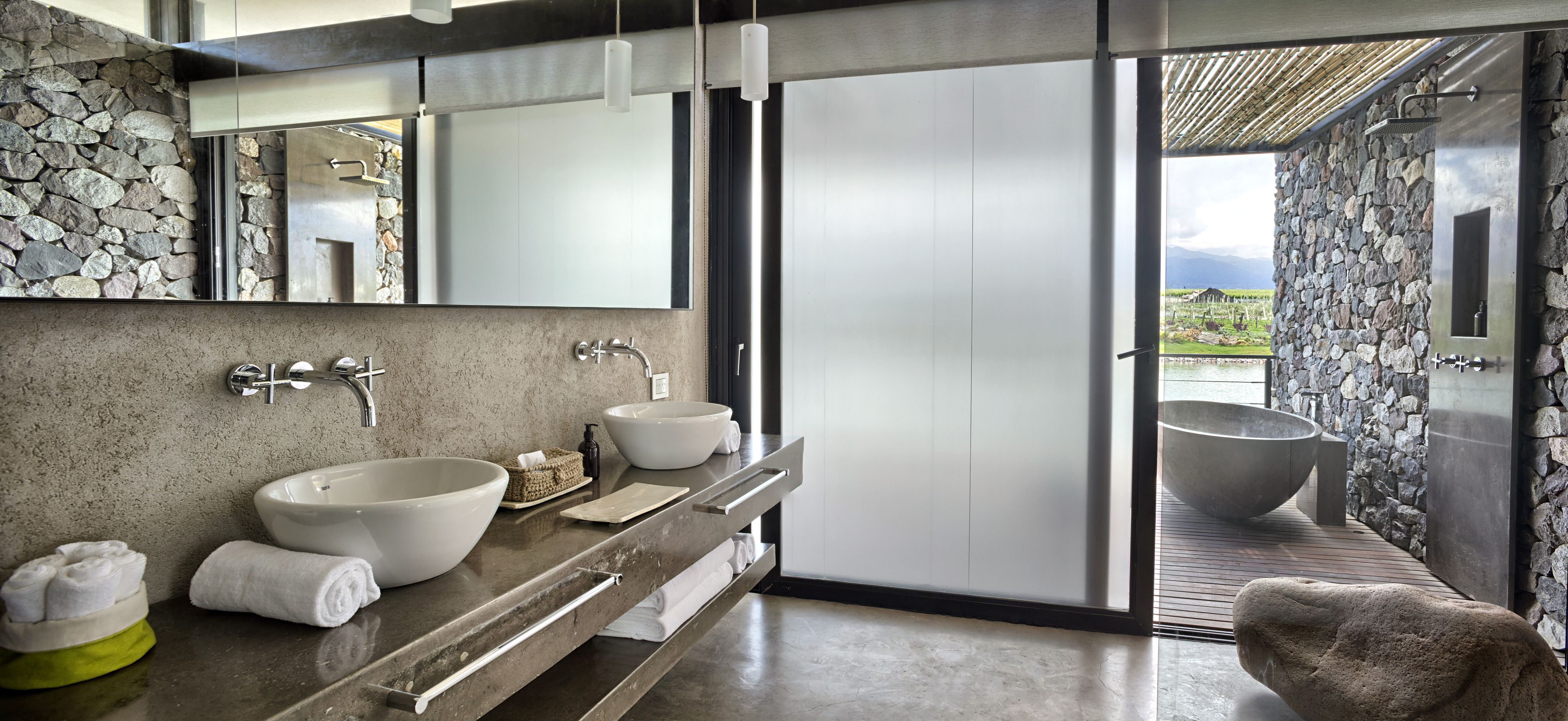 A modern bathroom with a stone wall, two sinks, a large bathtub, and a view of the outdoors.