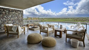 Un amplio espacio al aire libre con muros de piedra, mobiliario de madera y vistas a montañas y un lago.