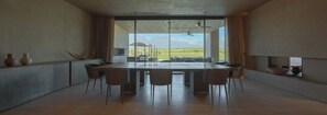 A modern dining area with a large table and chairs, large windows with a view of mountains, and a ceiling fan. - The Vines Resort & Spa (Tunuyan)