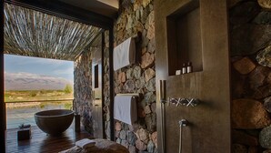 Un baño de paredes de piedra con un lavabo grande, ducha y vistas a la montaña.