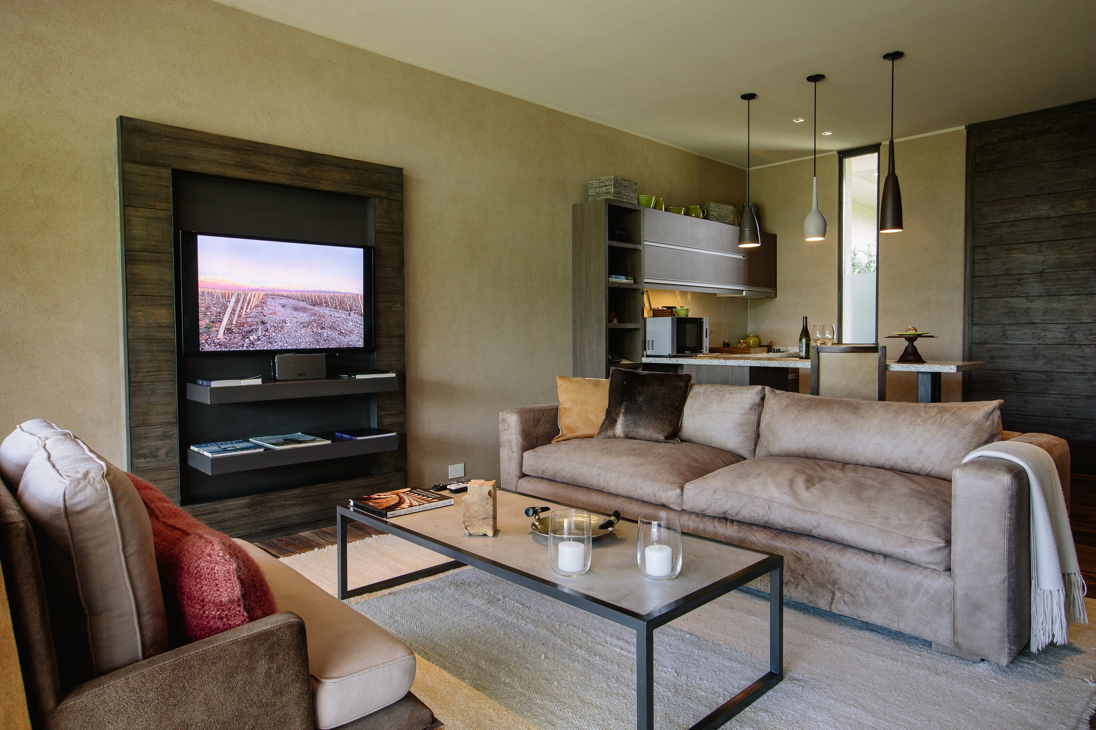 A modern living room with a flat-screen TV, a sofa, a coffee table, and a kitchen area in the background.