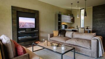 A modern living room with a flat-screen TV, a sofa, a coffee table, and a kitchen area in the background.