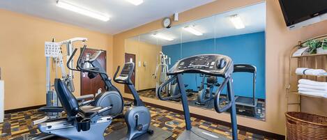 A gym with exercise equipment, a large mirror, a clock, and a TV on the wall.