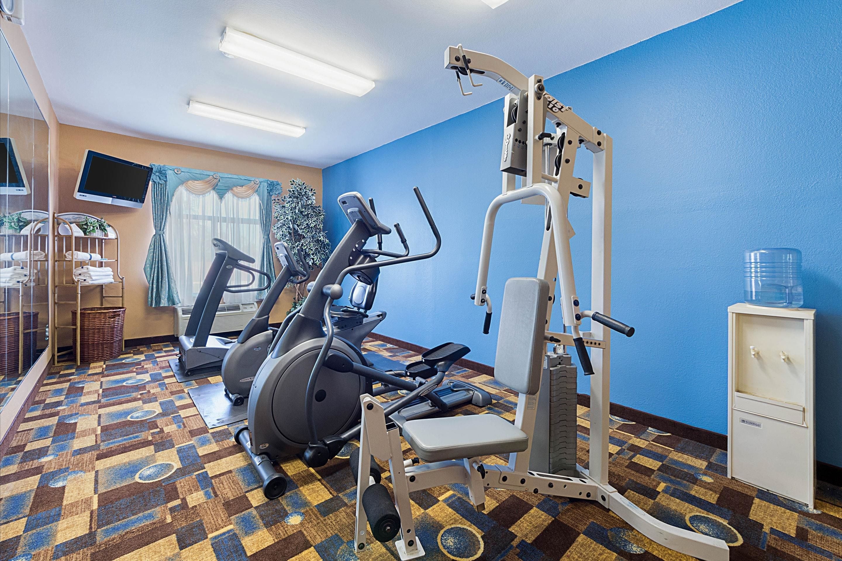 Une salle de remise en forme équipée de matériel d’exercice, d’un téléviseur et d’un distributeur d’eau.