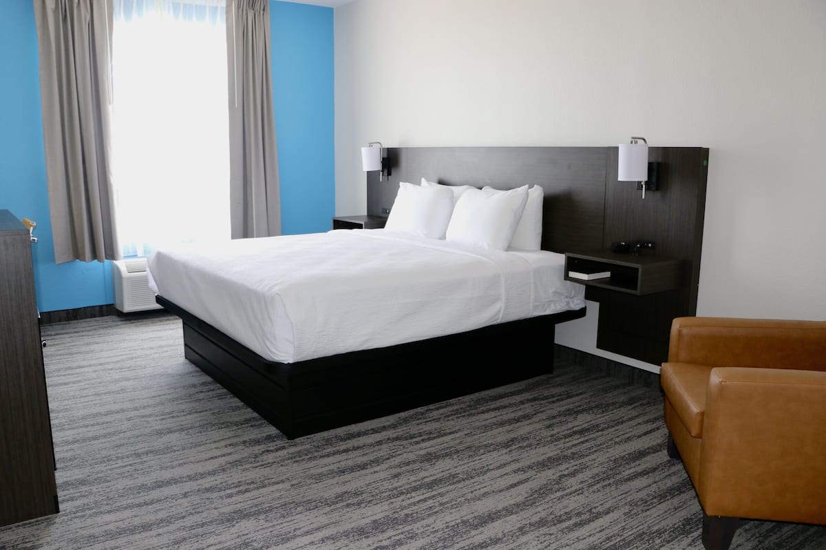 A hotel room with a large bed, two bedside tables, a nightstand, a brown leather chair, and a window with curtains.