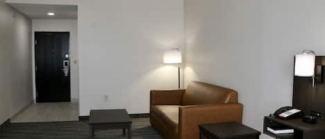 Une chambre d’hôtel avec un lit, un fauteuil en cuir marron, une petite table, une table de chevet avec un téléphone et une lampe.