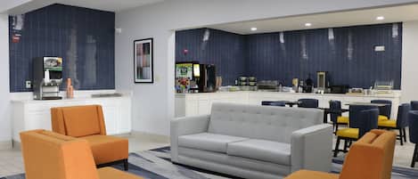 A modern living room with a grey sofa, orange armchairs, and a kitchen area with a blue tiled backsplash.
