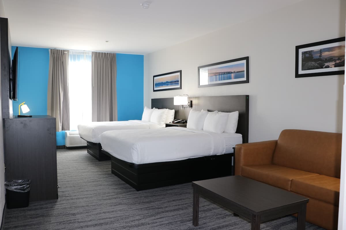 A hotel room with two beds, a sofa, a desk, and a TV.