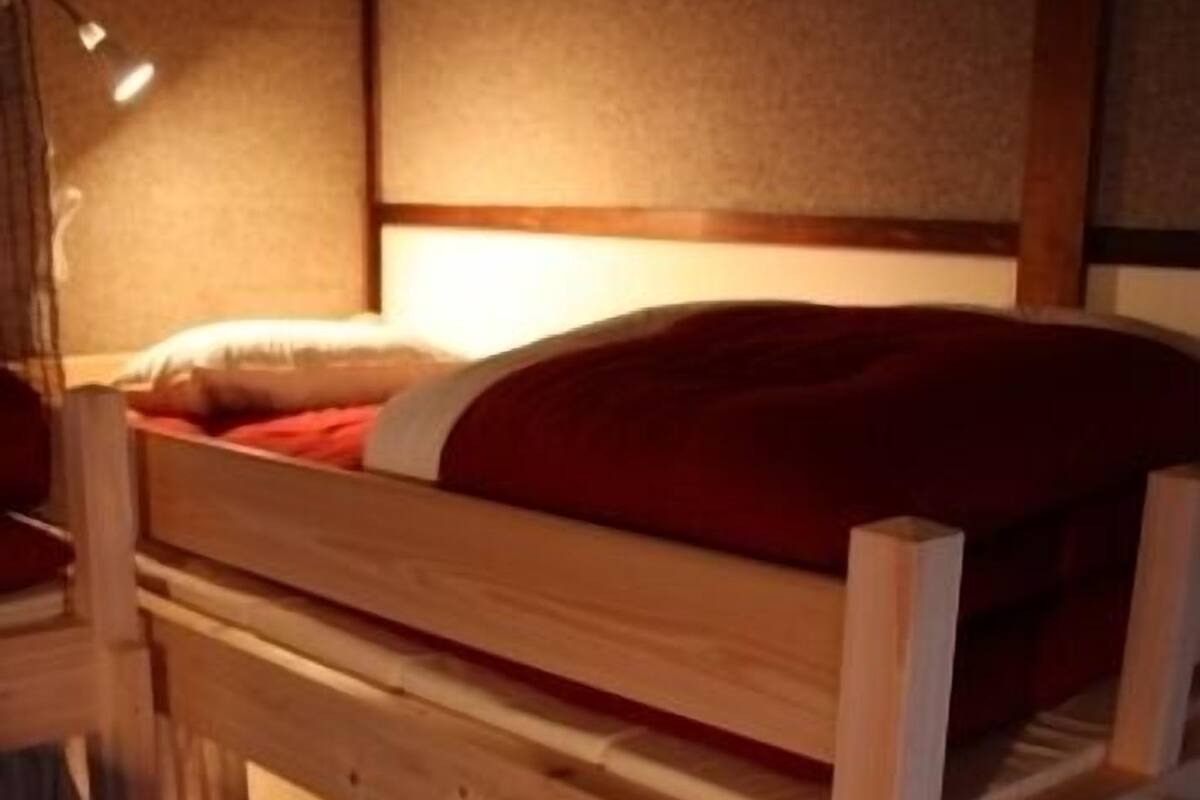 A bunk bed with a red blanket, a wooden ladder, and a lamp.