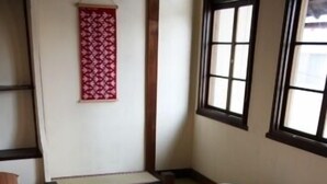 A room with a bed, pillows, a window, and a wall decoration. - Guesthouse Tomaru (Takayama)