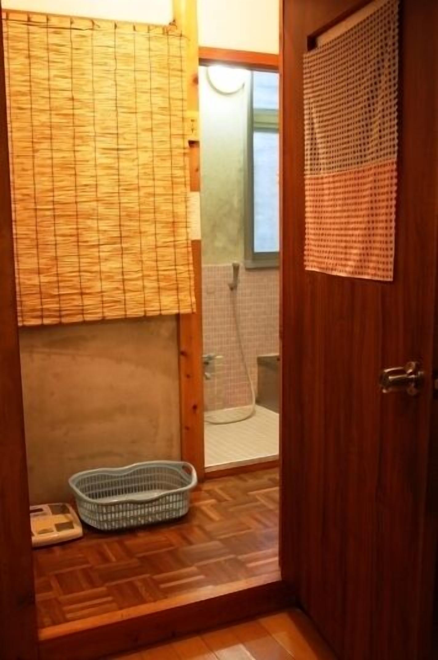 A wooden-floored bathroom with a bamboo blind, a small basket, and a shower area visible through a glass door.