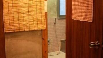 A wooden-floored bathroom with a bamboo blind, a small basket, and a shower area visible through a glass door.