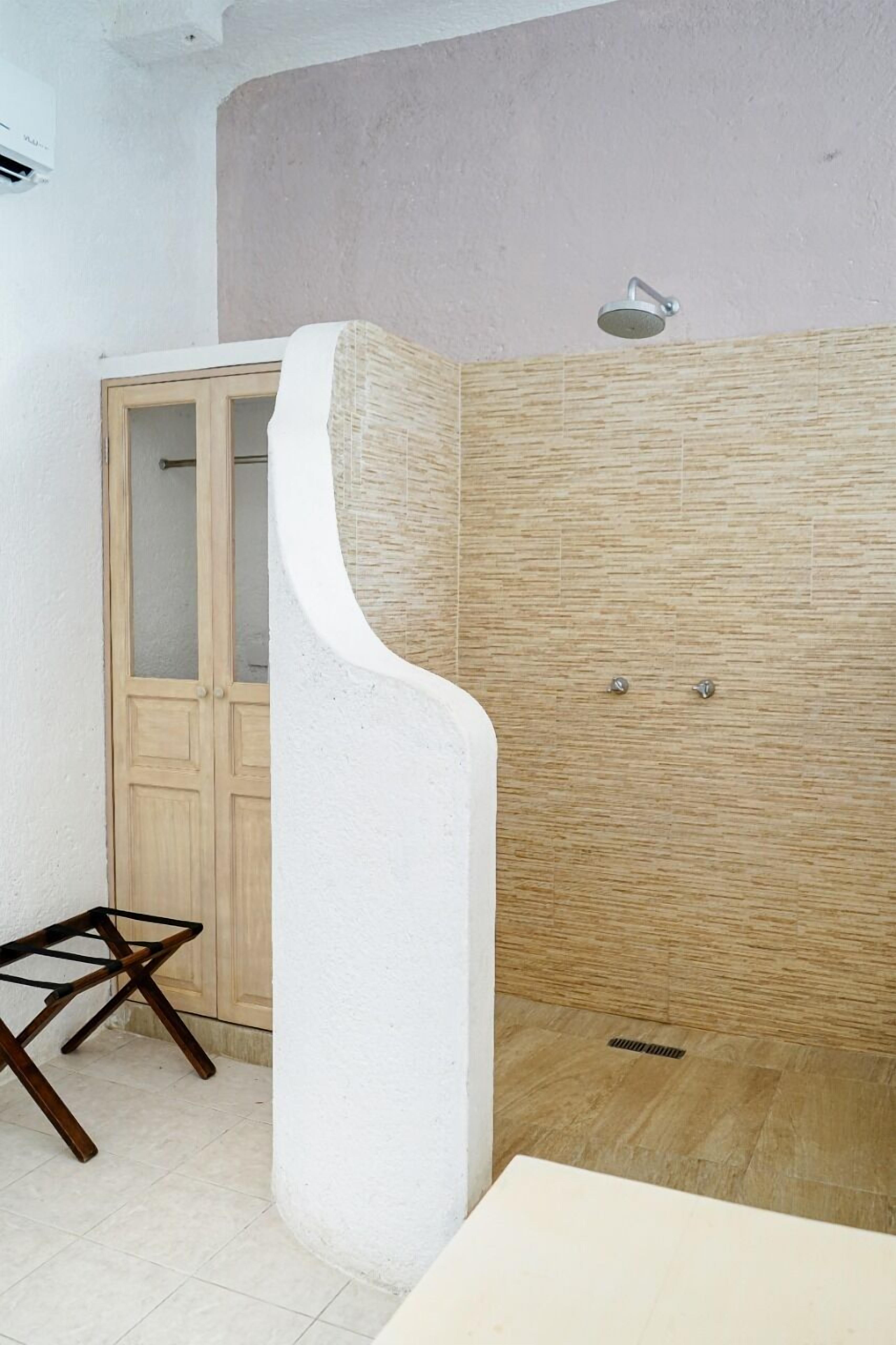 A bathroom with a shower, a wooden cabinet, and a white pillar.