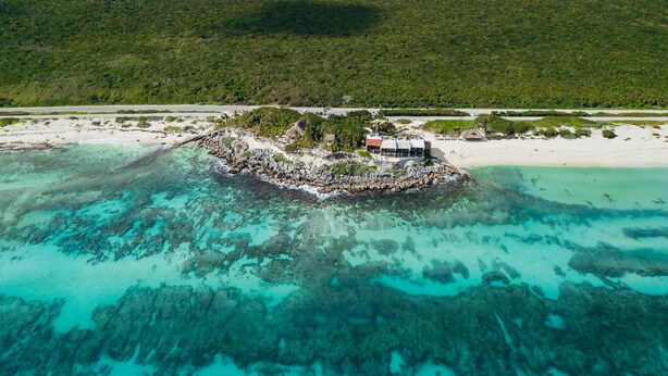 Vista aérea de una isla tropical con aguas turquesas cristalinas, una pequeña isla rocosa con un edificio y una playa.
