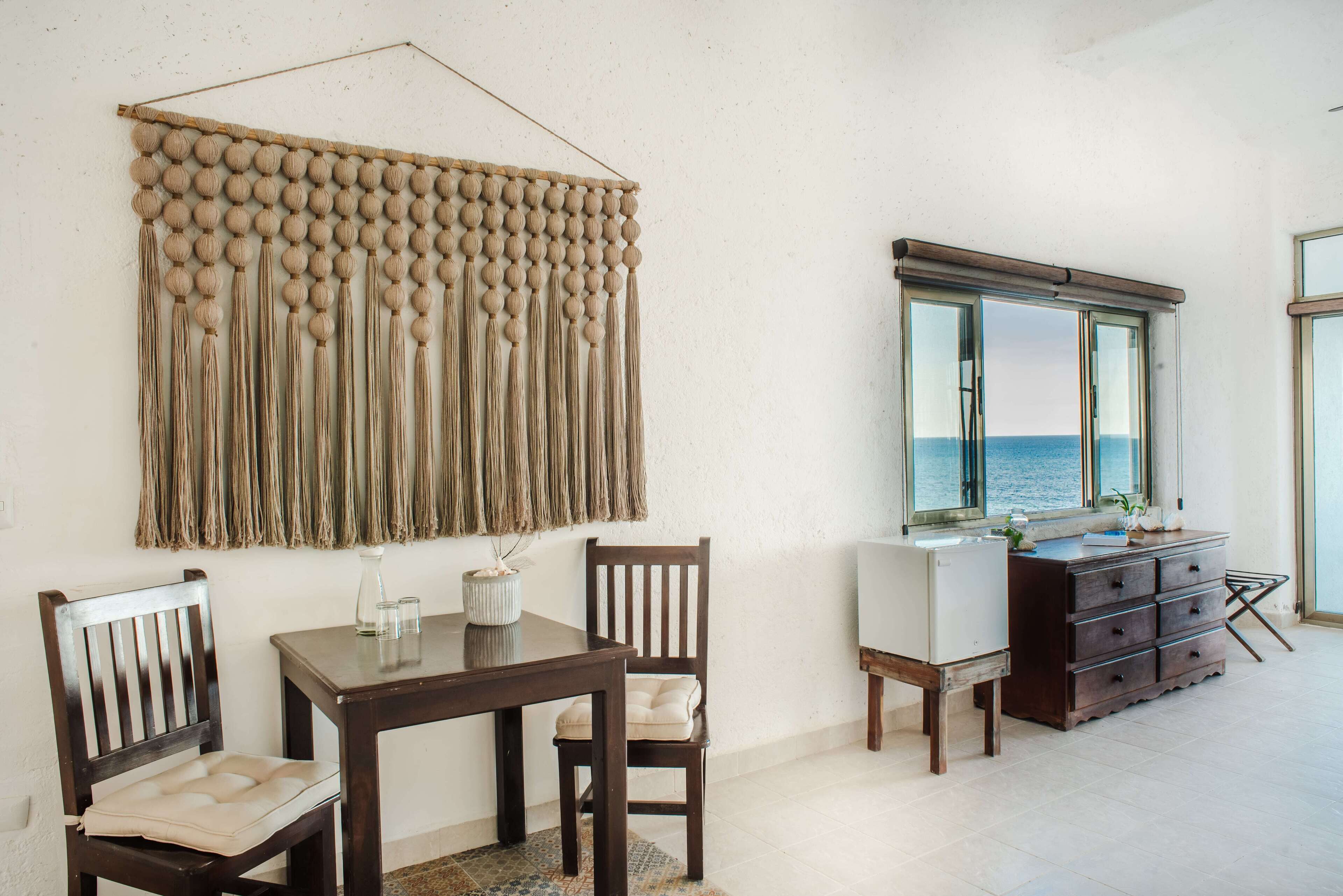 Un comedor con mesa y sillas de madera, un adorno en la pared y vista al mar a través de una ventana.