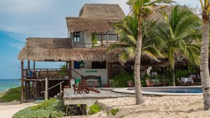 Una propiedad frente a la playa con una estructura de techo de paja, piscina y zona de arena.