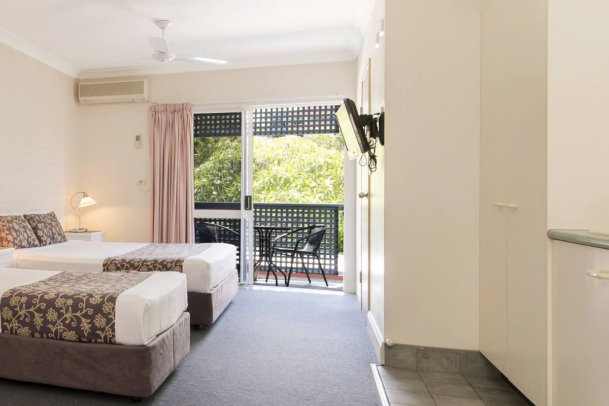 A hotel room with two beds, a purple sofa, a painting on the wall, and a balcony with a chair.
