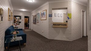 A reception area with a reception desk, a blue sofa, a glass table with a vase, and framed pictures on the walls. - Benson Court Motel (Toowong)