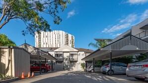A parking area with multiple cars, a building with a modern design, and a tall structure in the background. - Benson Court Motel (Toowong)