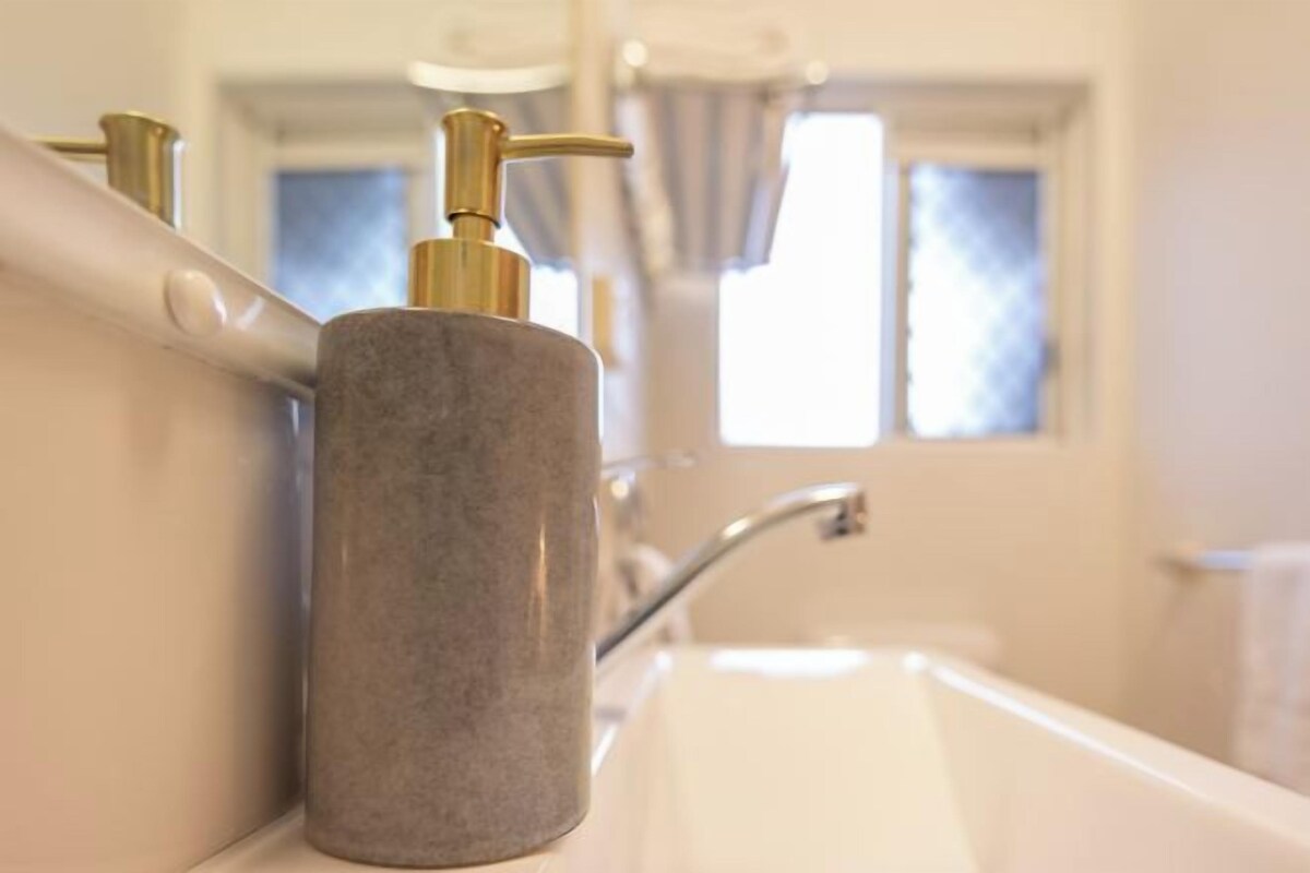 A bathroom with a white sink, a gold faucet, and a stone soap dispenser.